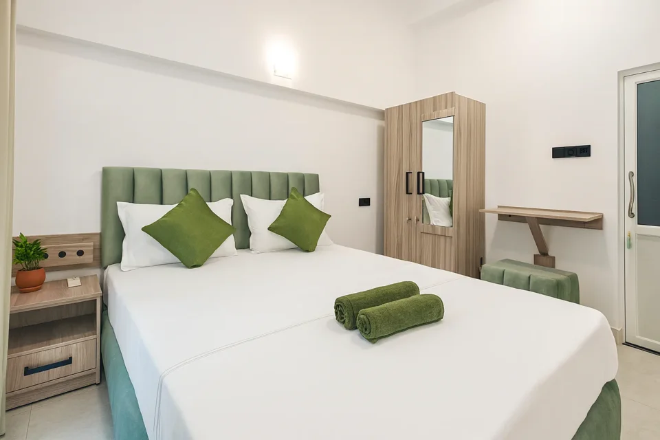 Ground-floor apartment bedroom with green headboard, white linen and wooden wardrobe