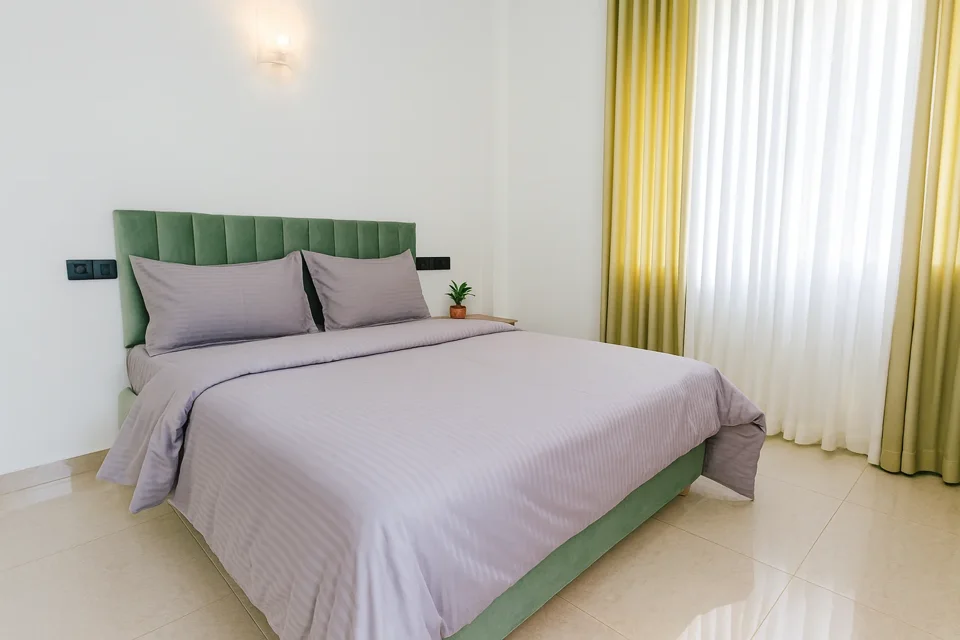 Katunayaka first-floor bedroom with grey bedding, a green headboard and yellow curtains