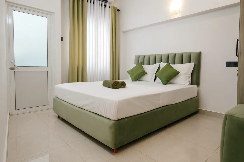 Ground-floor bedroom with a green upholstered bed, white linen and green cushions at Skyport Villa Katunayaka